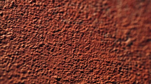 Close-up of textured brown wall surface with granular stucco finish under direct sunlight. Interior or exterior decoration.