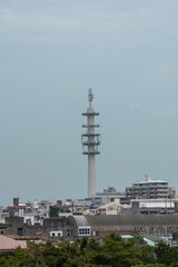 A towering communication structure rises amidst the cityscape, surrounded by urban buildings under an overcast sky.