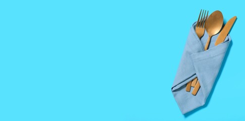 Napkin and golden cutlery on blue background with space for text