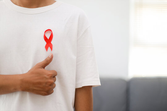 Man Wearing Red World AIDS Day Ribbon on His Chest With His Thumb Up in Support of HIV Positive People.