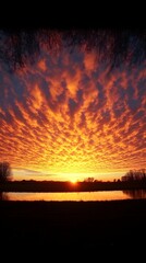 Vibrant sunset hues paint the sky, reflected in a calm river, silhouetted by dark trees