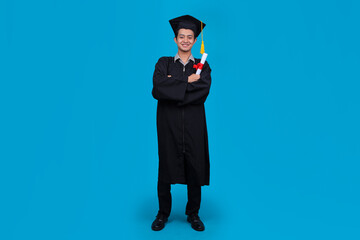Smiling Asian Student in Graduation Attire Stands With Certificate in Hand