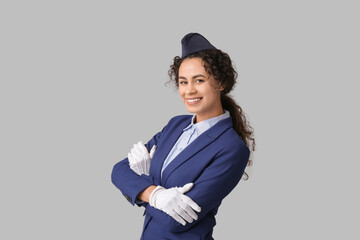 Beautiful young African-American stewardess on grey background