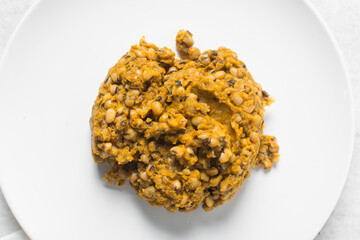 Overhead view of nigerian fried beans on a white plate, top view of nigerian stewed beans on a white background	