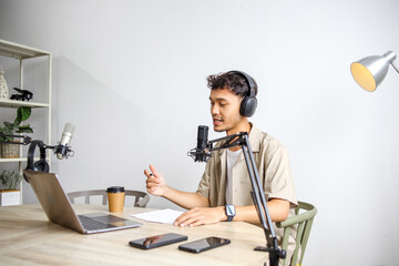 Young Host Recording Online Podcast Using Laptop, Headphones and Professional Microphone.
