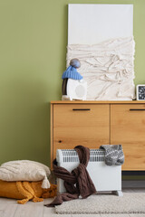Wooden cabinet with modern electric heaters and decor near green wall