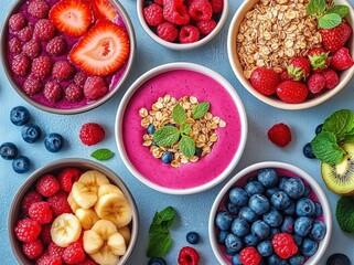 Colorful assortment of fresh berries, sliced banana, granola, and vibrant smoothie bowls garnished with mint leaves displayed on a blue surface