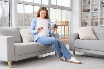 Young pregnant woman with dried prunes sitting on sofa at home