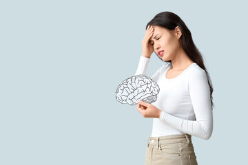 Young Asian woman with paper brain suffering from headache on grey background. Brain Injury Awareness Month