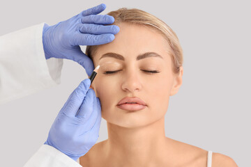 Plastic surgeon marking woman's face against light background, closeup. Blepharoplasty concept