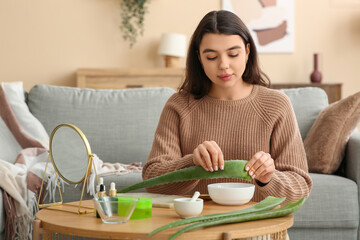 Young woman making organic cosmetics with aloe vera near table in living room