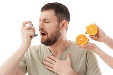 Young man using asthma inhaler and female hands with orange on white background. Food Allergy...