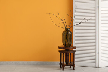Interior of room with folding screen, stool and vase with twigs near yellow wall, closeup