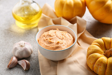 Bowl of tasty hummus with pumpkins and garlic on grey background