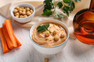 Bowl of tasty hummus with carrot, peas and parsley on white background