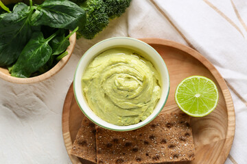 Bowl of tasty peas hummus with lime, spinach and crackers on white background