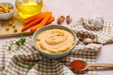 Bowl of tasty hummus with carrot, microgreen and garlic on pink background