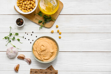 Bowl of tasty hummus with chickpeas, microgreen and garlic on white wooden background