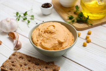 Bowl of tasty hummus with garlic and crackers on white wooden background