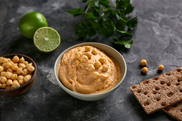 Bowl of tasty hummus with limes, parsley, crackers and chickpeas on black grunge background