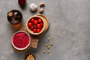 Bowl of tasty beet hummus with tomatoes, garlic, chickpeas and crackers on grey background