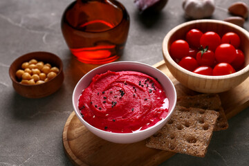 Bowl of tasty beet hummus with tomatoes, chickpeas and crackers on grey background