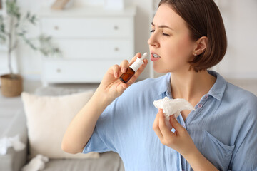 Allergic young woman with tissue using nasal drops at home