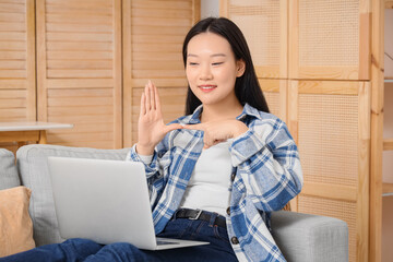 Mute Asian woman using sign language during video call at home