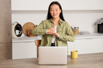 Mute Asian woman using sign language during video call at home