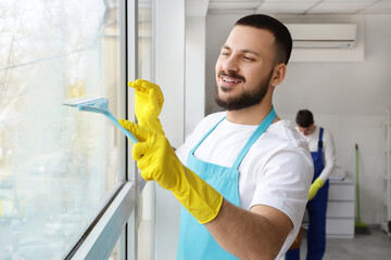 Male janitor cleaning window in office