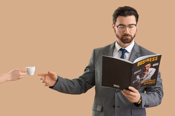 Handsome businessman with magazine taking coffee cup from hand on beige background