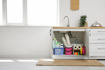 Baskets and bucket with different cleaning supplies and paper towels under sink in kitchen