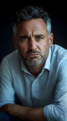 Obraz premium Close-up portrait of a serious, middle-aged man with graying hair and blue eyes, wearing a light-colored shirt, against a dark background