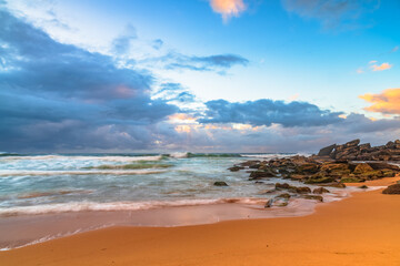 Sunrise at the seaside with rocks and rain clouds