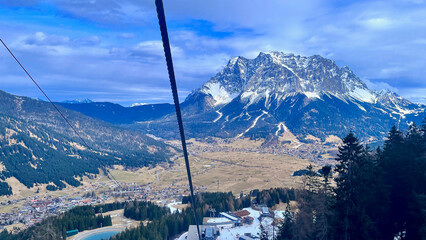 Vast mountain landscape with snowy peaks, valley town, and ski lift wires.