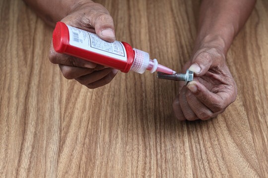 A Male Engineers hand applying a drop of Thread Lock fluid (loctite 271) to the Thread of a bolt before assembling.