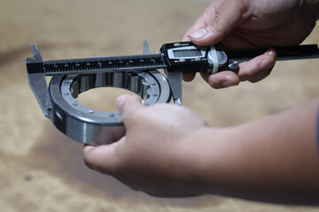 Worker is measuring outside diameter of bearing with a digital vernier caliper micrometer....