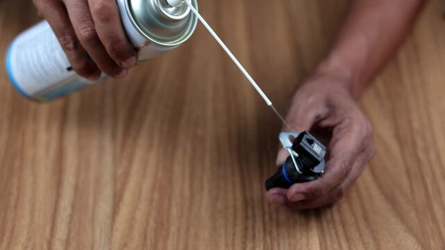 Close up hand Spray the transmission speed sensor with contact cleaner, to clean and repair it on wooden table.
