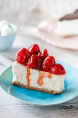 Piece of cheesecake with strawberries and jam on plate on light wooden background. Sweets, dessert and pastry, close up