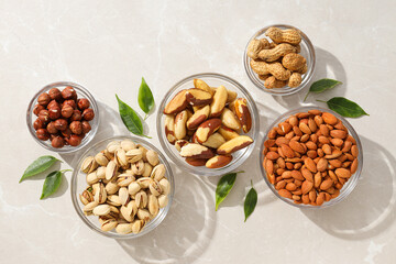 Different types of nuts in transparent glass bowls on a white background