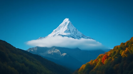Fototapeta premium Majestic Snow-Capped Mountain Rises Above Colorful Autumn Foliage Under a Clear Blue Sky at Sunrise