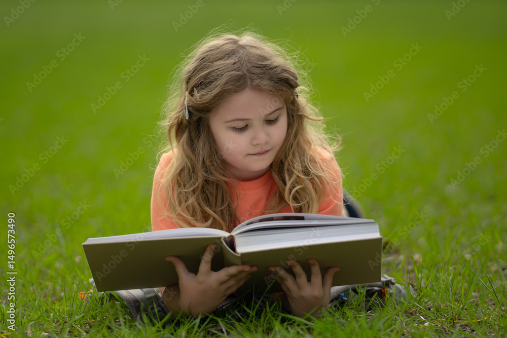 Poster child reading a book in the grass. child enjoying a book story outdoors. child studying with book in