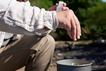 Unrecognizable male traveler seasoning his food, cooking outdoors while camping at a nature campground a sunny morning. Close up view of the hand that pours the salt.