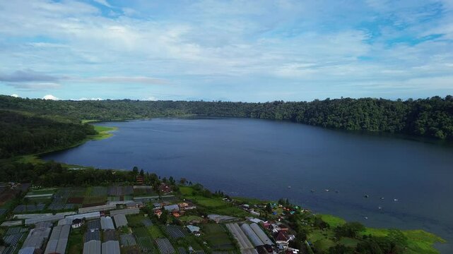 Experience breathtaking aerial views of Lake Tamblingan, a hidden gem in Bali, surrounded by traditional lakeside houses nestled among vibrant tropical greenery. 