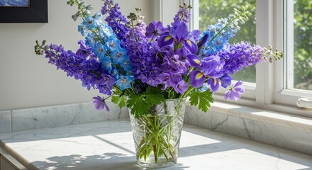 Fototapeta premium Photo of Purple and Blue Delphiniums and Irises in Crystal Vase by Sunny Window