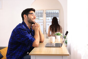 Business couple working, communicating while sitting at the home office desk together. Cheerful couple, calm asian woman and caucasian man working at home with laptop together.
