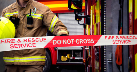Firefighter in action at fire scene cordon with hand of fireman reaching for emergency services fire truck door. Two fire engine appliances and smoke billowing through the air at the event.