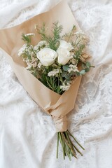 Bouquet of white roses with greenery wrapped in craft paper on a lace surface
