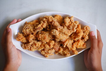 Hand holding a plate of fried chicken 