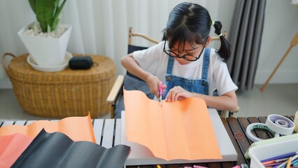 Asian girl focused on making a DIY craft project at home using a compass and colorful paper, promoting creativity, fine motor skills, and fun learning in a homeschool setting.
